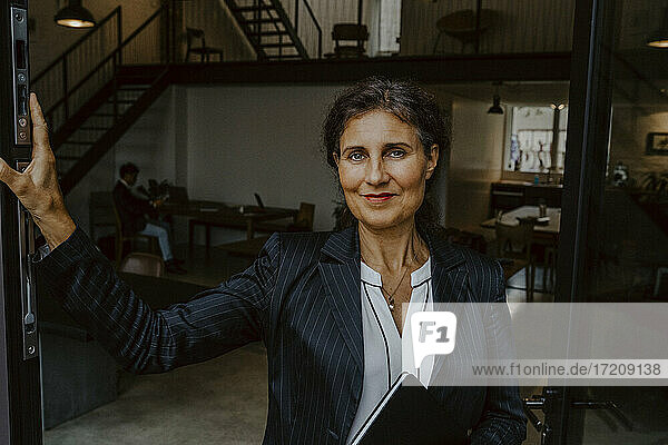 Portrait of businesswoman leaning at doorway in office