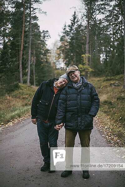 Portrait of senior gay couple standing on road amidst forest