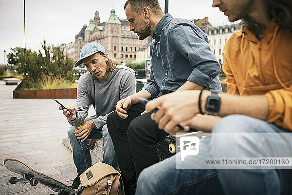 Männliche Skater  die das Smartphone benutzen  während sie auf dem Gehweg sitzen