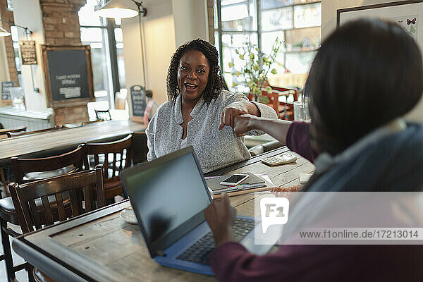 Businesswomen fist bumping at laptop in cafe