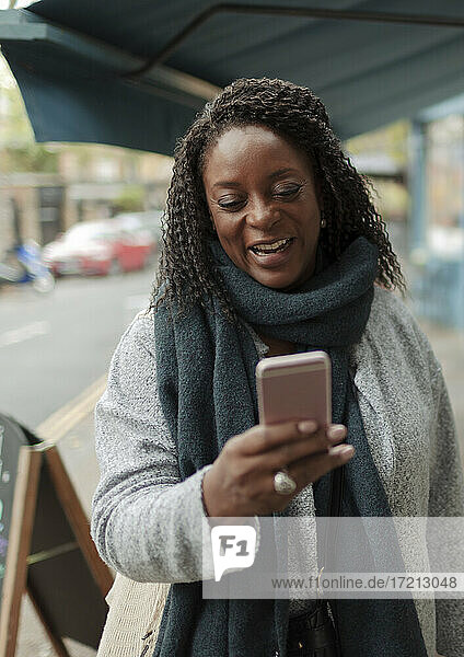 Happy woman in scarf using smart phone on sidewalk