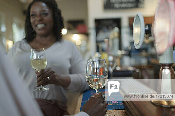 Happy woman drinking white wine with friend in bar