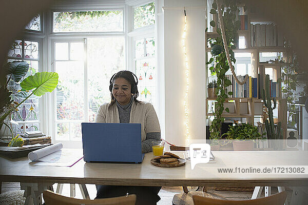 Frau mit Kopfhörer arbeitet von zu Hause aus am Laptop
