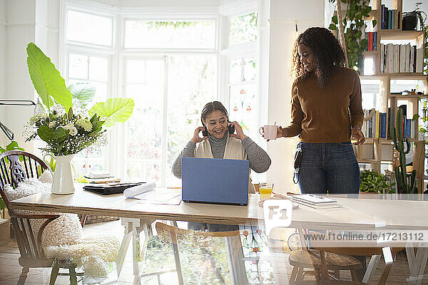 Daughter serving coffee to mother working at laptop on dining table