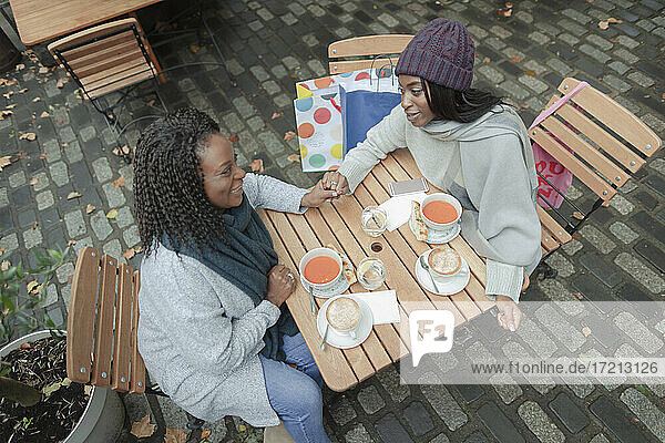 Mutter und Tochter halten die Hände und genießen das Mittagessen im Straßencafé