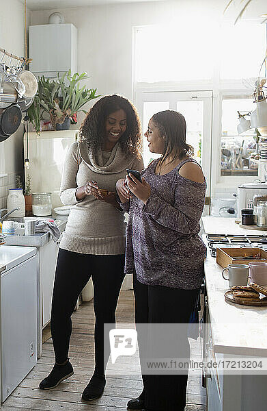 Mutter und Tochter verwenden Smartphones in der Küche
