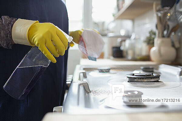Frau in Gummihandschuhen reinigt Küchenherd mit Sprühreiniger