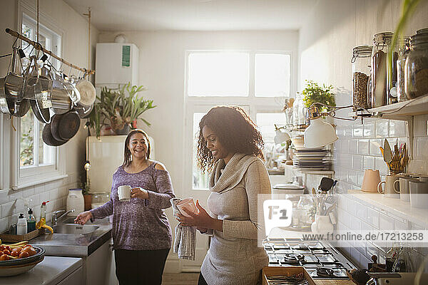 Mother and daughter doing dishes in apartment kitchen