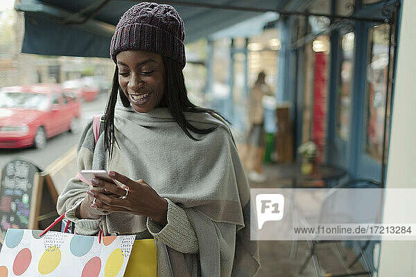 Junge Frau mit Einkaufstasche mit Smartphone auf dem Bürgersteig
