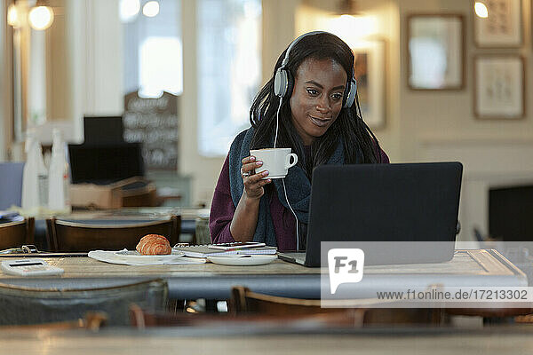 Junge Frau mit Kopfhörer trinken Kaffee am Laptop im Café