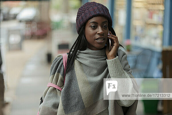 Stilvolle junge Frau spricht auf Smartphone auf dem Bürgersteig