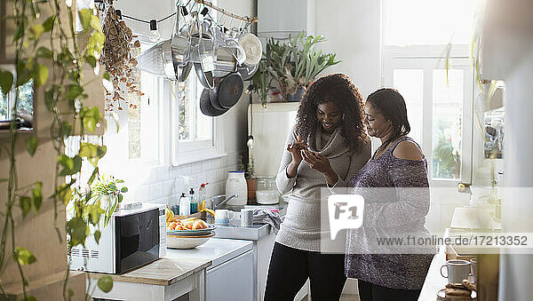 Mutter und Tochter verwenden Smartphones in der Küche