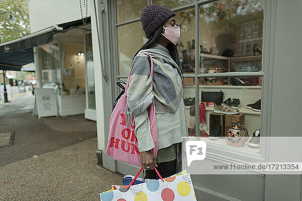 Junge Frau mit Gesichtsmaske und Einkaufstüten vor einem Geschäft
