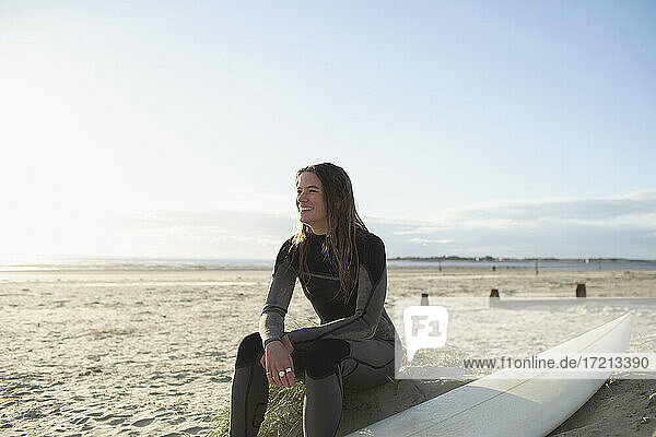 Happy young female surfer resting with surfboard on sunny beach