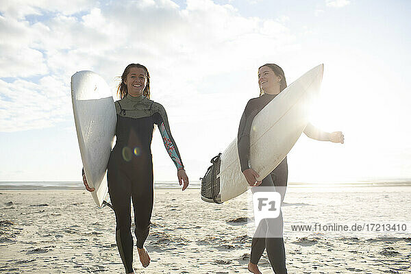 Glückliche junge Surferinnen laufen mit Surfbrettern am sonnigen Strand