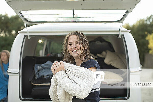 Portrait happy young woman putting on sweater outside camper van