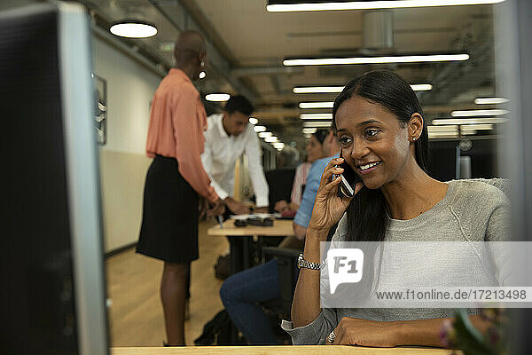 Lächelnde Geschäftsfrau spricht auf Smartphone in Großraumbüro