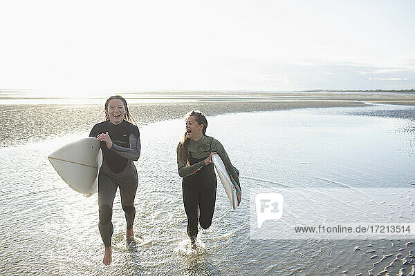 Sorglose junge Surferinnen laufen mit Surfbrettern im sonnigen Ozean