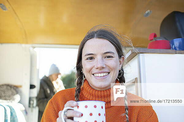Porträt glückliche junge Frau trinkt Tee in Wohnmobil Türöffnung