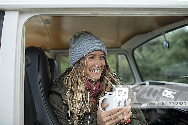 Glückliche junge Frau trinkt Kaffee im Wohnmobil Türöffnung