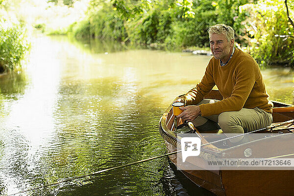Happy man fly fishing and drinking coffee in boat on river
