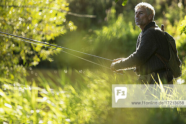Mann mit Rucksack Fliegenfischen mit Stock unter sonnigen Gras