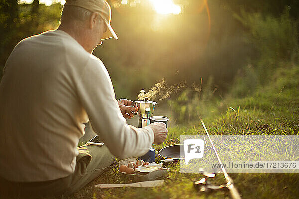 Mann macht Pause von der Fliegenfischerrute und kocht Kaffee am Flussufer