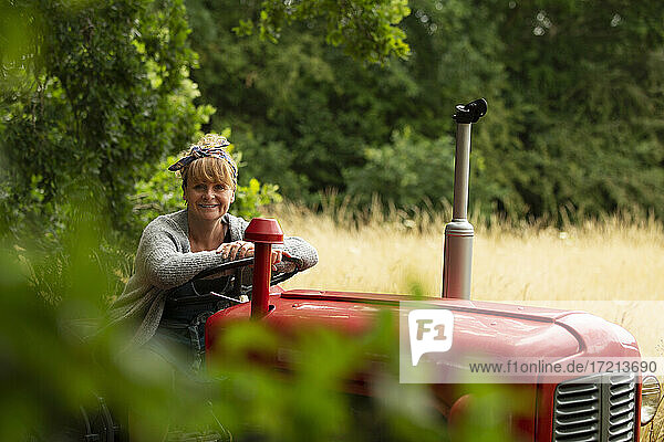 Porträt glückliche Frau fährt Traktor im Obstgarten