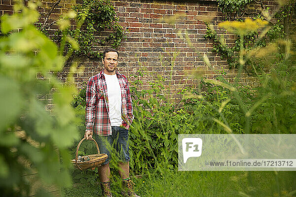 Porträt selbstbewusster Mann mit Korb an Backsteinmauer im Sommergarten