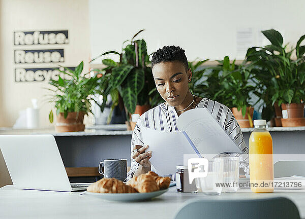 Businesswoman reviewing paperwork at breakfast in office lounge