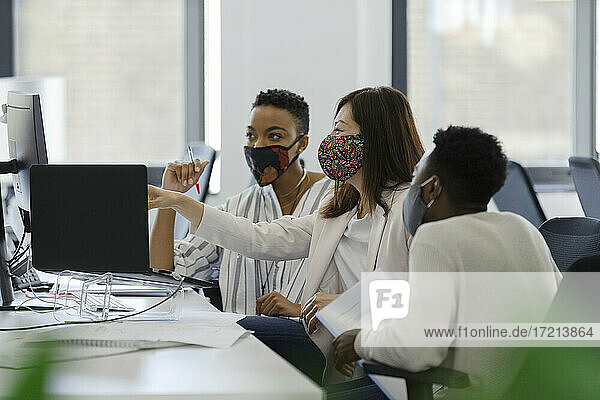Geschäftsleute in Gesichtsmasken arbeiten am Computer im Büro