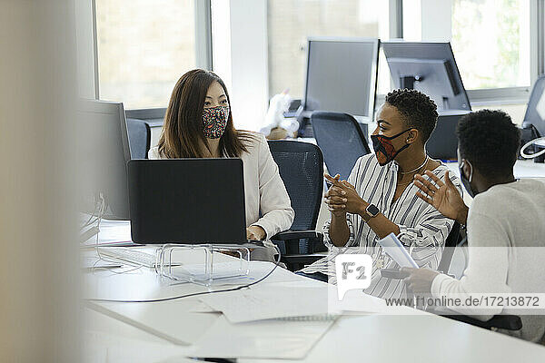 Geschäftsleute in Gesichtsmasken im Gespräch im Büro Sitzung