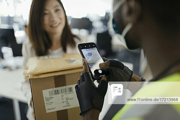 Businesswoman receiving packages from courier with smart phone