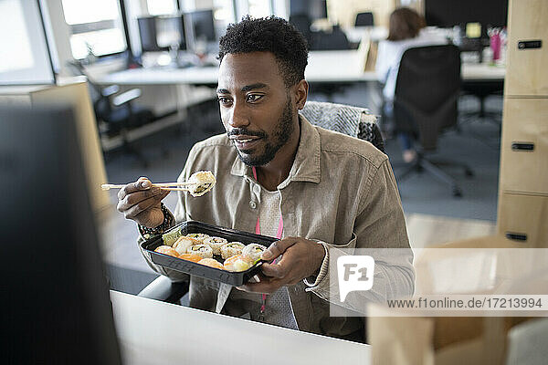 Businessman eating sushi takeout lunch at computer in office