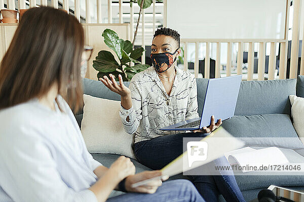 Businesswomen in face masks meeting on office sofa