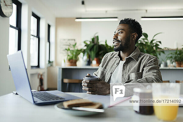 Thoughtful businessman with coffee working at laptop in office