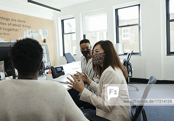 Business people in face masks talking in office meeting
