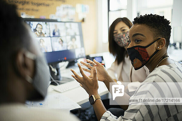 Business people in face masks video conferencing at computer in office
