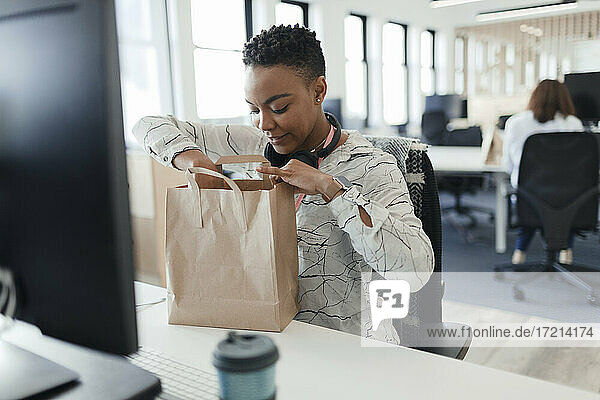 Businesswoman opening takeout lunch bag at desk in office