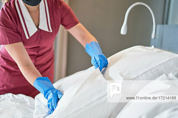Hotelmädchen mit Handschuhen beim Bettenmachen im Hotelzimmer