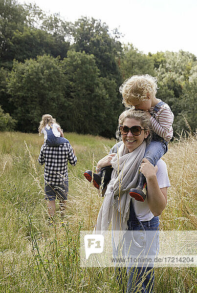 Portrait happy mother carrying daughter on shoulders in rural field