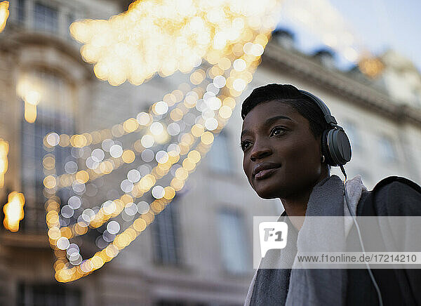 Selbstbewusste junge Frau mit Kopfhörer unter Gebäude mit Lichtern