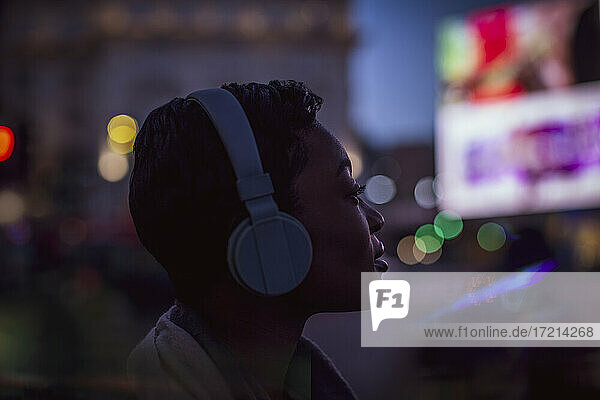 Junge Frau mit Kopfhörern auf Stadtstraße mit Lichtern in der Nacht