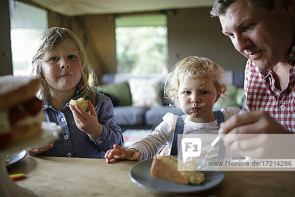 Father and daughters eating cake at dining table