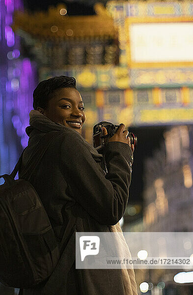 Porträt glückliche junge Frau mit Kamera in der Stadt bei Nacht