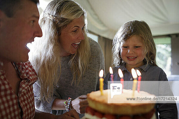 Glückliche Tochter feiert Geburtstag mit Familie und Kuchen mit Kerzen