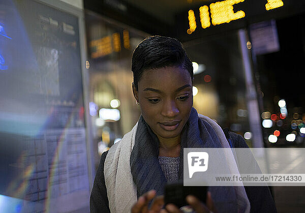 Young woman using smart phone at urban bus stop at night