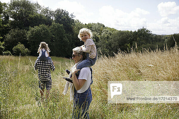 Porträt glücklich niedlichen Mädchen auf den Schultern der Mutter in sonnigen ländlichen Feld