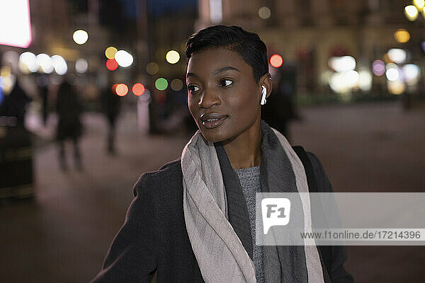Young woman with earbud headphones on city street at night