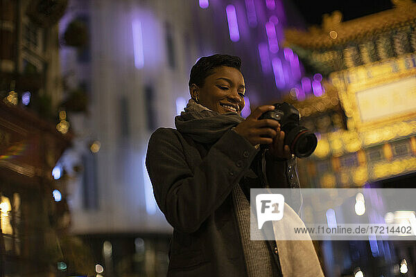 Smiling young woman with camera on city street at night